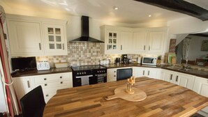 A kitchen with white cabinets, a wooden island, a stove, and a microwave. - Historic detached cottage, on the banks of the River Severn Nr Upton & Malvern (Worcestershire)