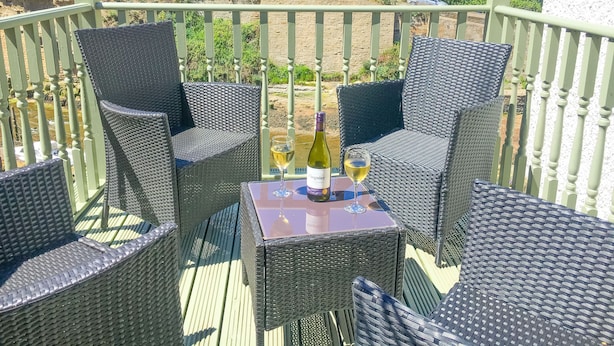 A balcony with wicker furniture and a table with a bottle of wine and a glass.