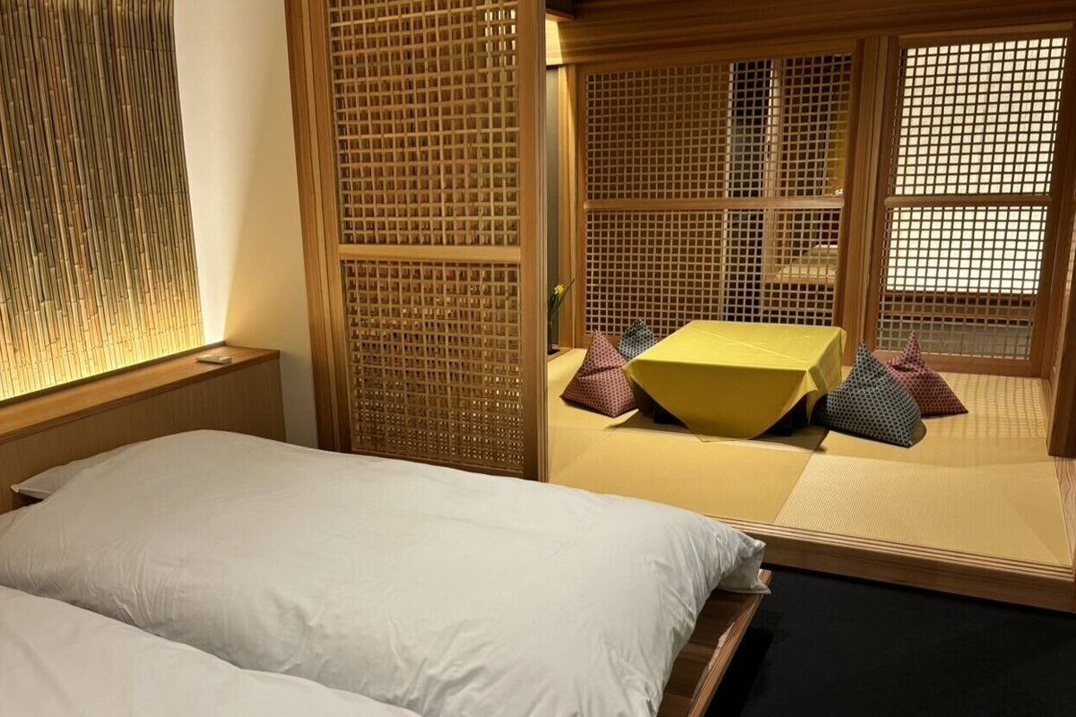 A traditional Japanese-style room with tatami flooring, a low wooden bed, and a sliding door with a lattice design.