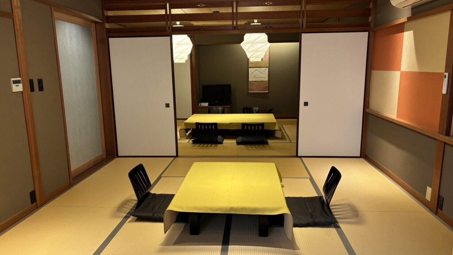 A traditional Japanese room with tatami flooring, a low table with a yellow tablecloth, black chairs, and sliding doors.