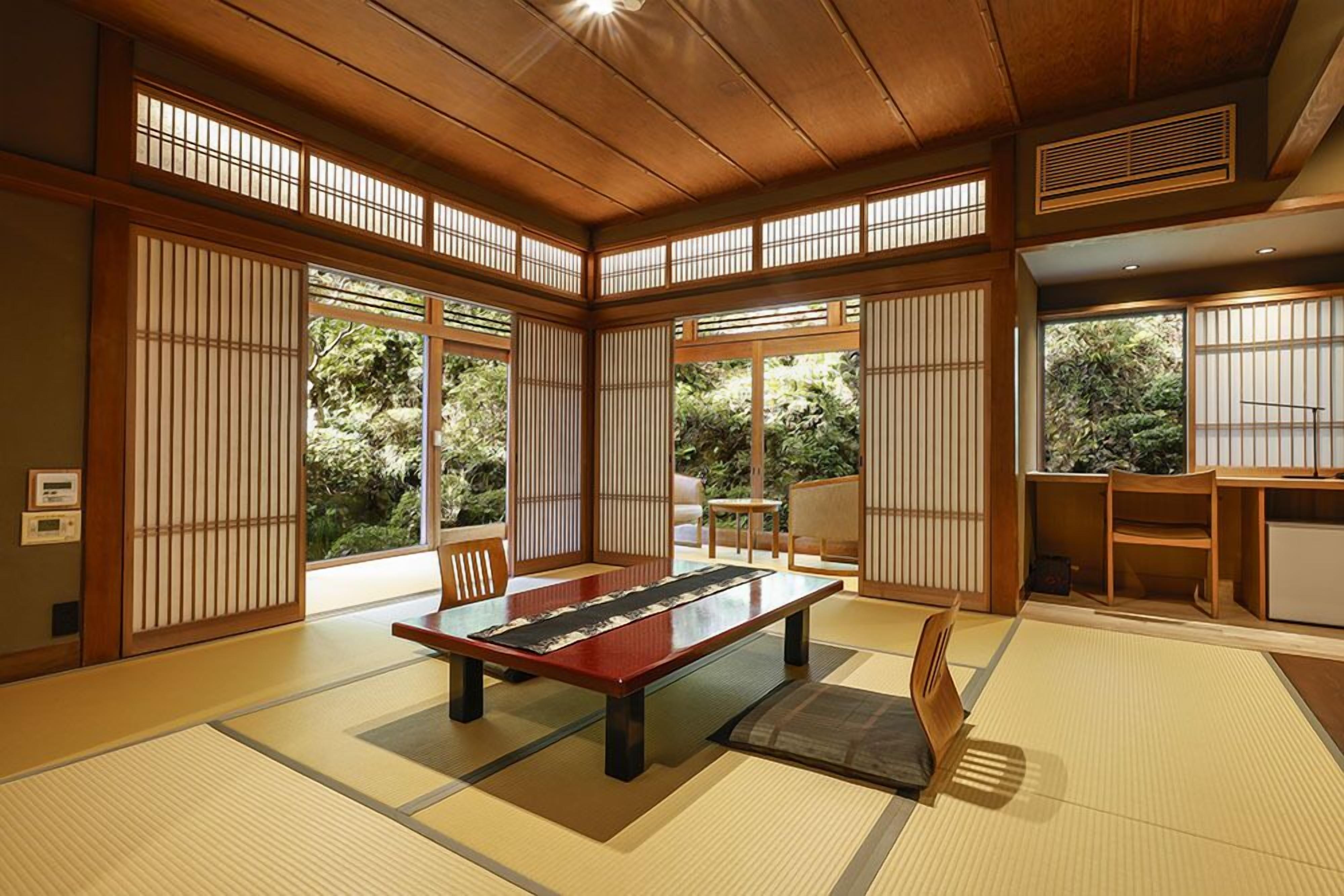 Een traditionele Japanse kamer met tatami vloerbedekking, een lage tafel, schuifdeuren en uitzicht op groen buiten.