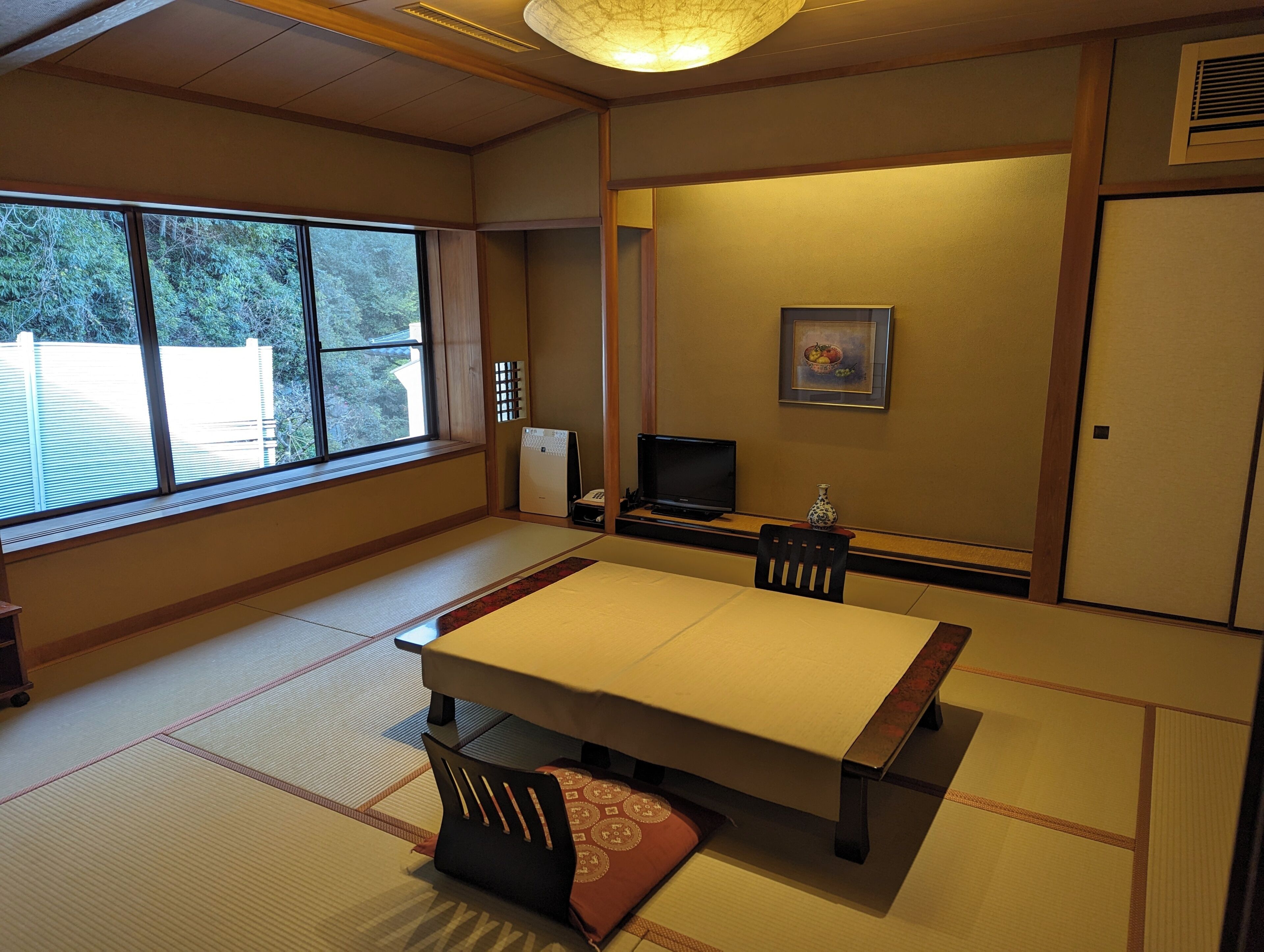 A traditional Japanese room with tatami flooring, a low table, a television, and a painting on the wall.