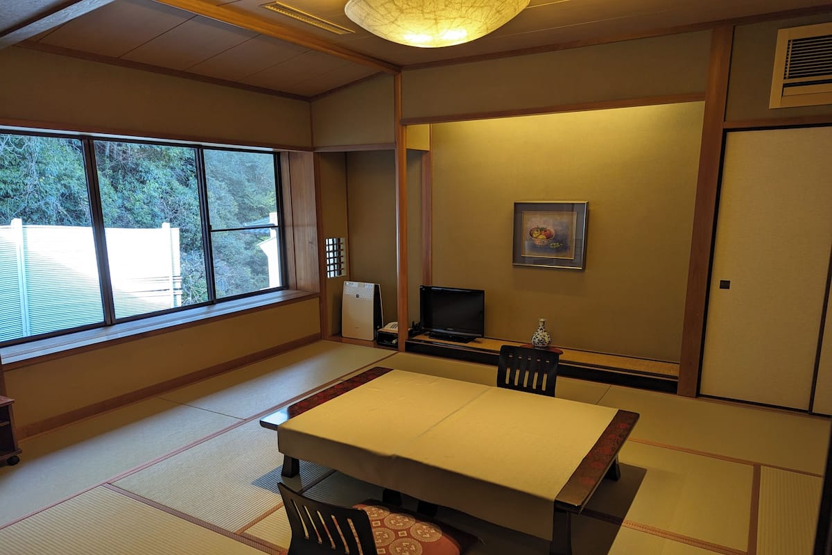 A traditional Japanese room with tatami flooring, a low table, a television, and a painting on the wall.