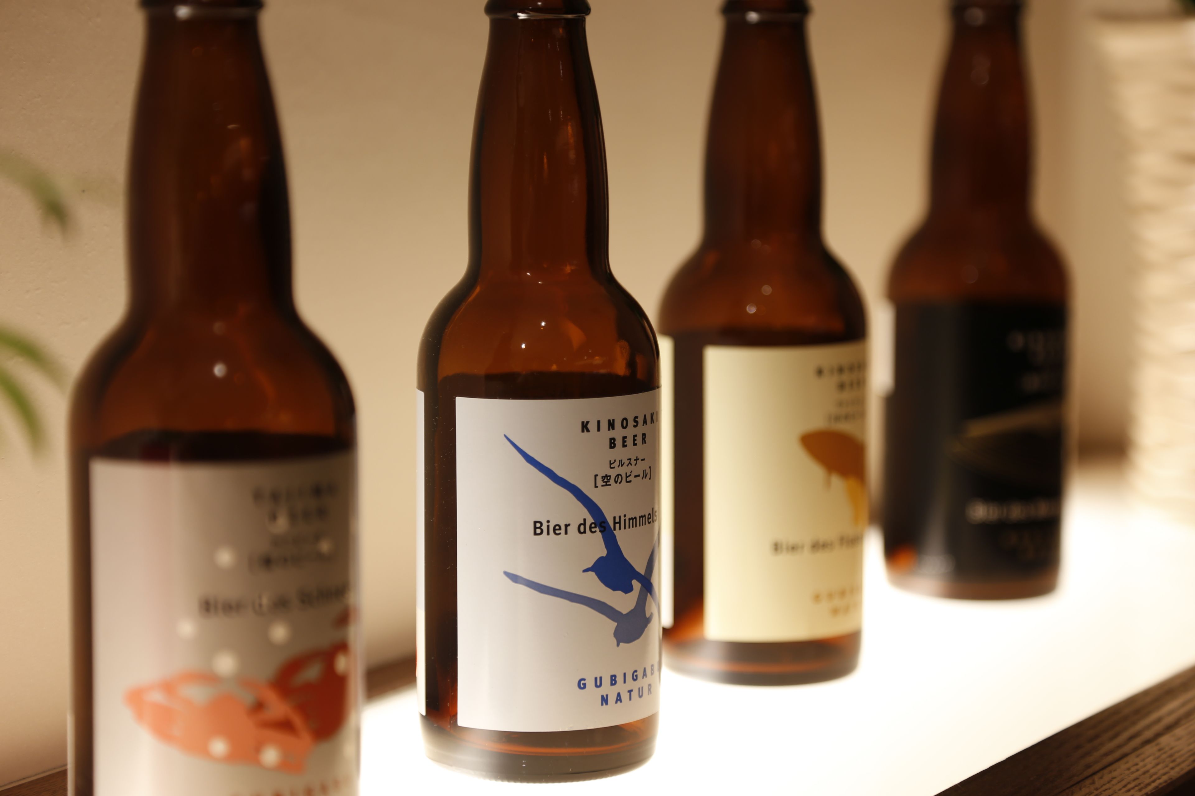 Quatre bouteilles de bière, avec leurs étiquettes, disposées sur une étagère.