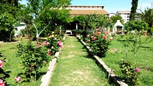Un chemin de jardin bordé de rosiers qui mène à un bâtiment doté d’un toit en tuiles.