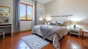 Une chambre à coucher comprenant un lit, des tables de chevet, une commode, une fenêtre avec des rideaux, un miroir et un tapis.