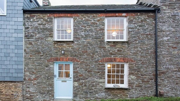 A stone building with a blue door and two windows with white frames.