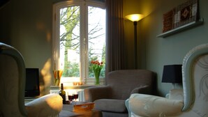 Un salon avec deux fauteuils, une petite table, un lampadaire et une fenêtre donnant sur des arbres.