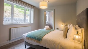 Un dormitorio con una cama grande, una ventana, un radiador y una mesita de noche con una lámpara.