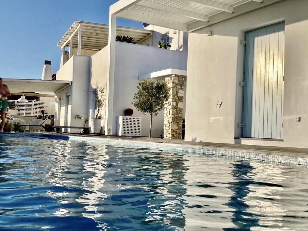 A modern pool area with clear blue water, a stone pillar, and a white building with a blue door.