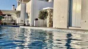 A modern pool area with clear blue water, a stone pillar, and a white building with a blue door.