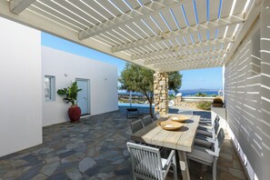 A covered outdoor seating area with stone flooring, a table with chairs, and a view of the sea. - VILLA GALAZIO, PRIVATE POOL, SEA VIEWS AND SUNSETS OVER ANTIPAROS (Paros)