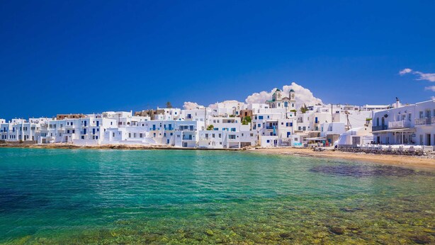 A coastal town with white buildings, clear turquoise water, and a rocky shoreline.