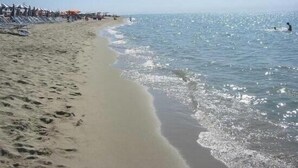En strand med klar himmel, en sandstrand och ett lugnt hav.