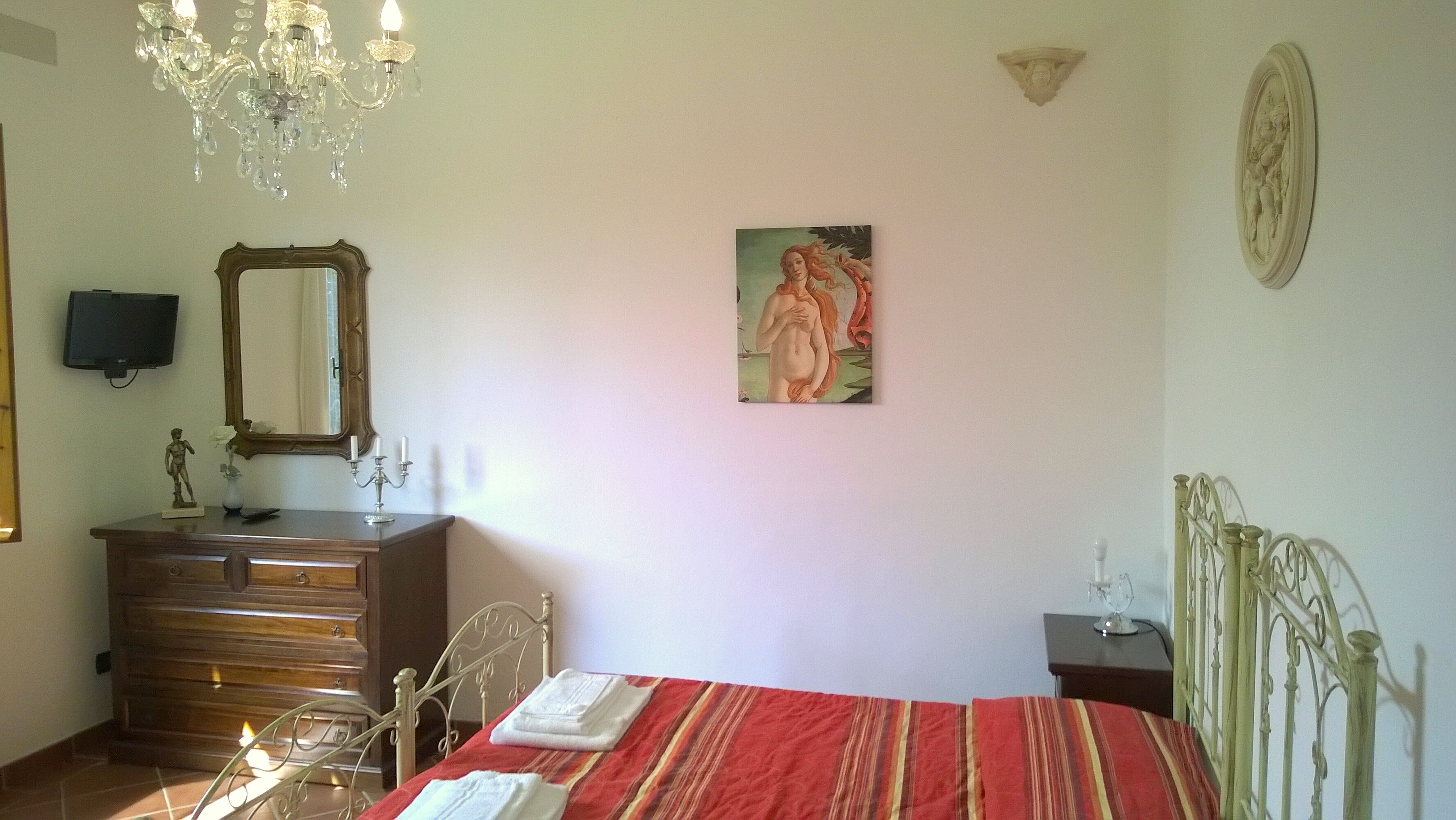 A bedroom with a bed, a dresser, a mirror, a chandelier, and a painting on the wall.