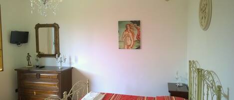 A bedroom with a bed, a dresser, a mirror, a chandelier, and a painting on the wall.
