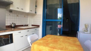 Une cuisine de taille réduite avec des meubles blancs, un plan de travail en bois et une table recouverte d’une nappe jaune.