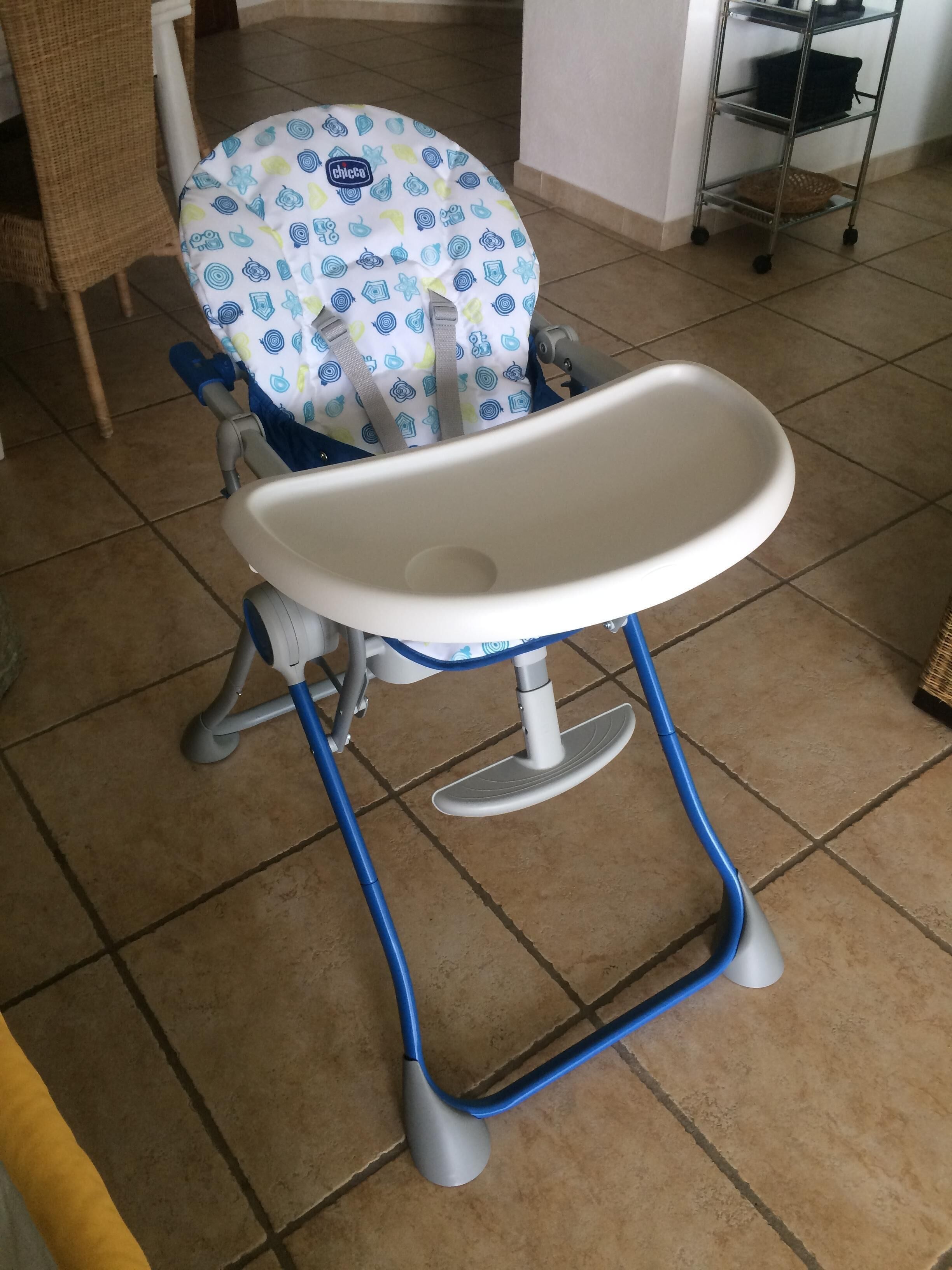 A baby high chair with a white tray and blue legs, placed on a tiled floor.