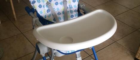 A baby high chair with a white tray and blue legs, placed on a tiled floor.