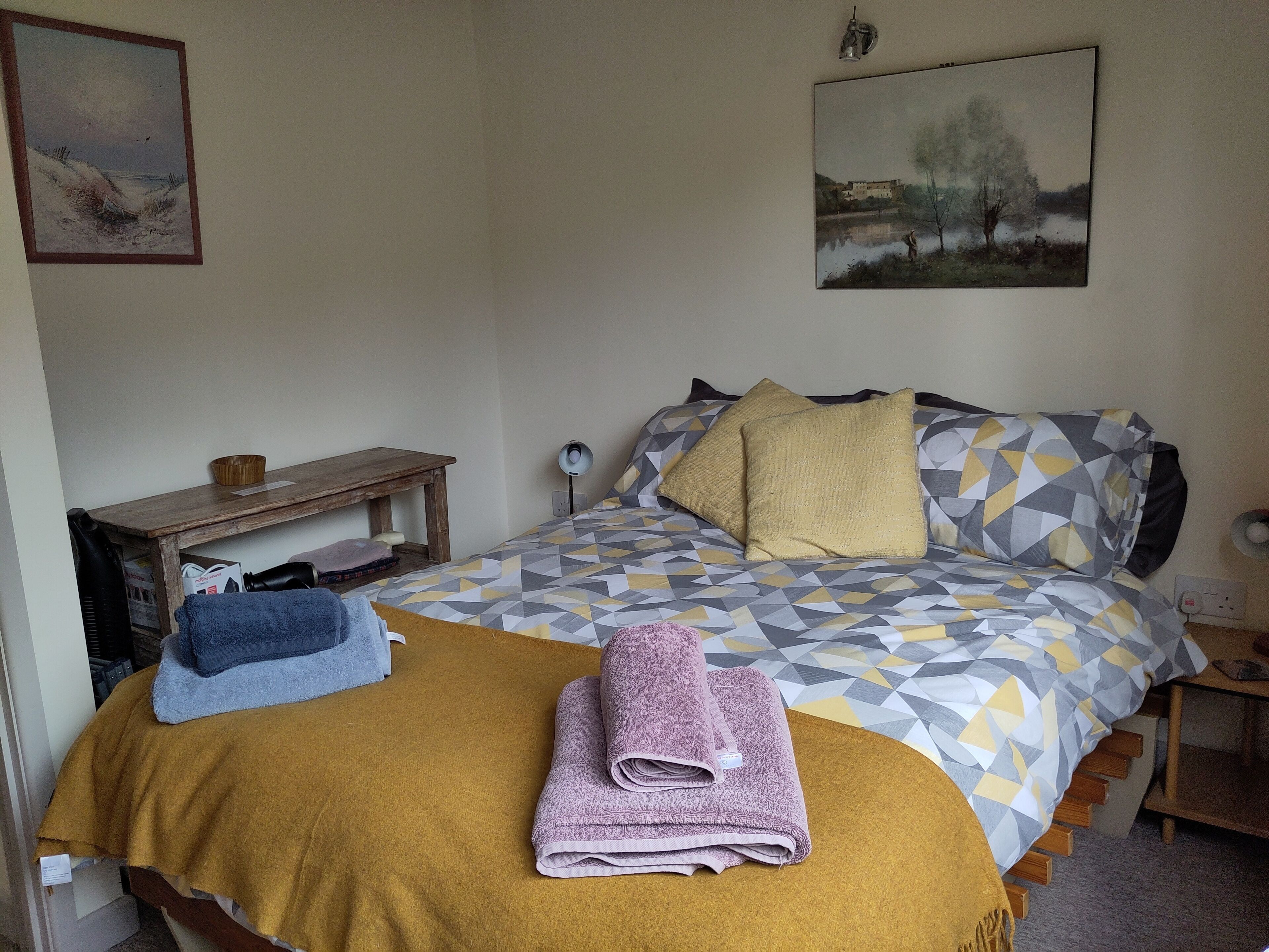 Ein Schlafzimmer mit einem Bett, einem Nachttisch aus Holz, einer Lampe und einem Bild an der Wand.