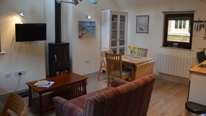 A cozy living room with a fireplace, dining table, and sofa. - Unique detached holiday cottage, Hampshire  (Sopley)