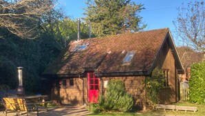 A rustic wooden cabin with a red door, a chimney, and a small window. - Unique detached holiday cottage, Hampshire  (Sopley)
