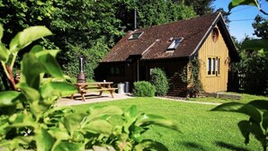 A rustic cabin with a sloped roof, a chimney, and a picnic table in a lush green setting. - Unique detached holiday cottage, Hampshire  (Sopley)