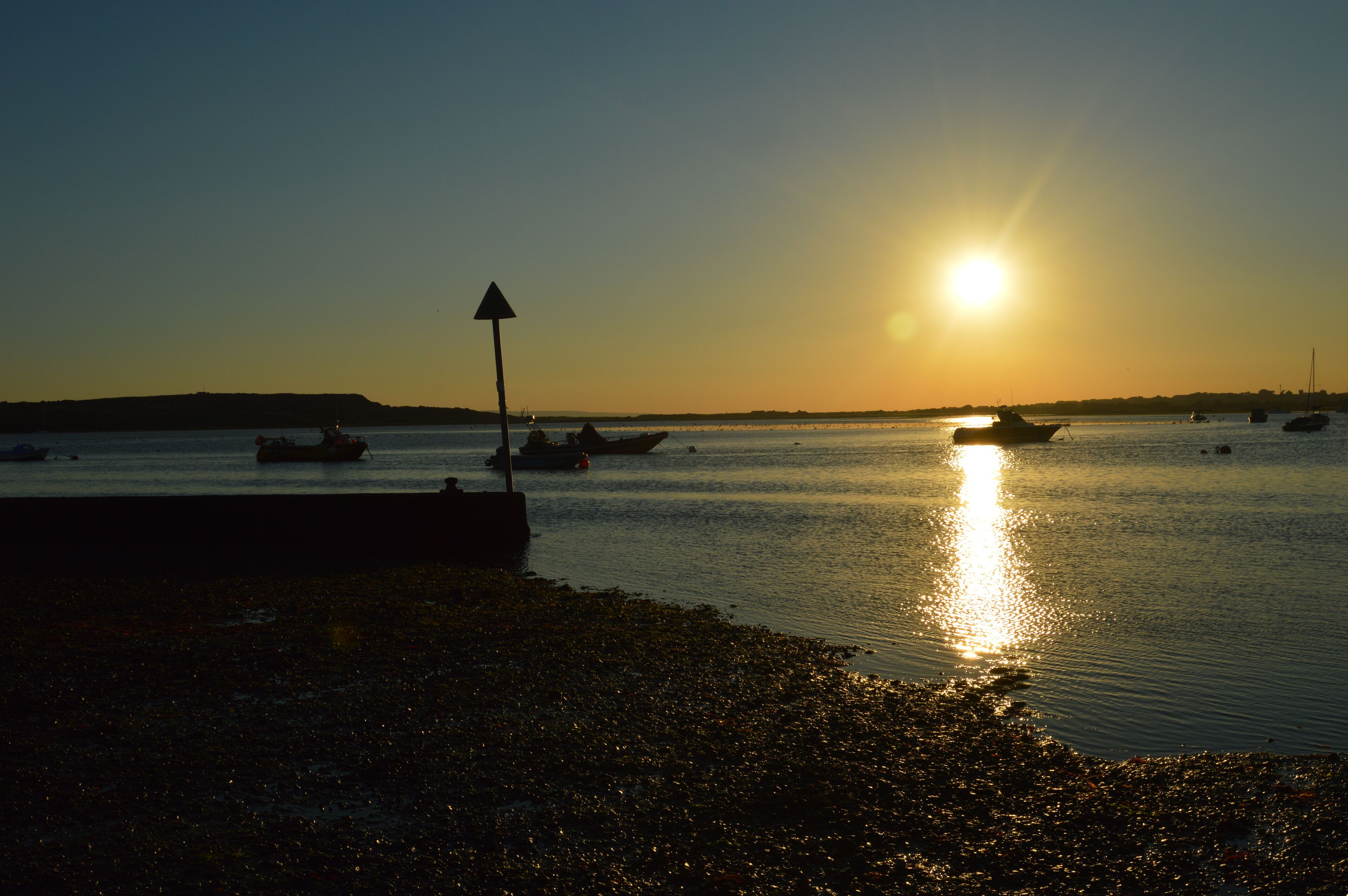 Um pôr do sol sobre águas calmas, com barcos e um cais.