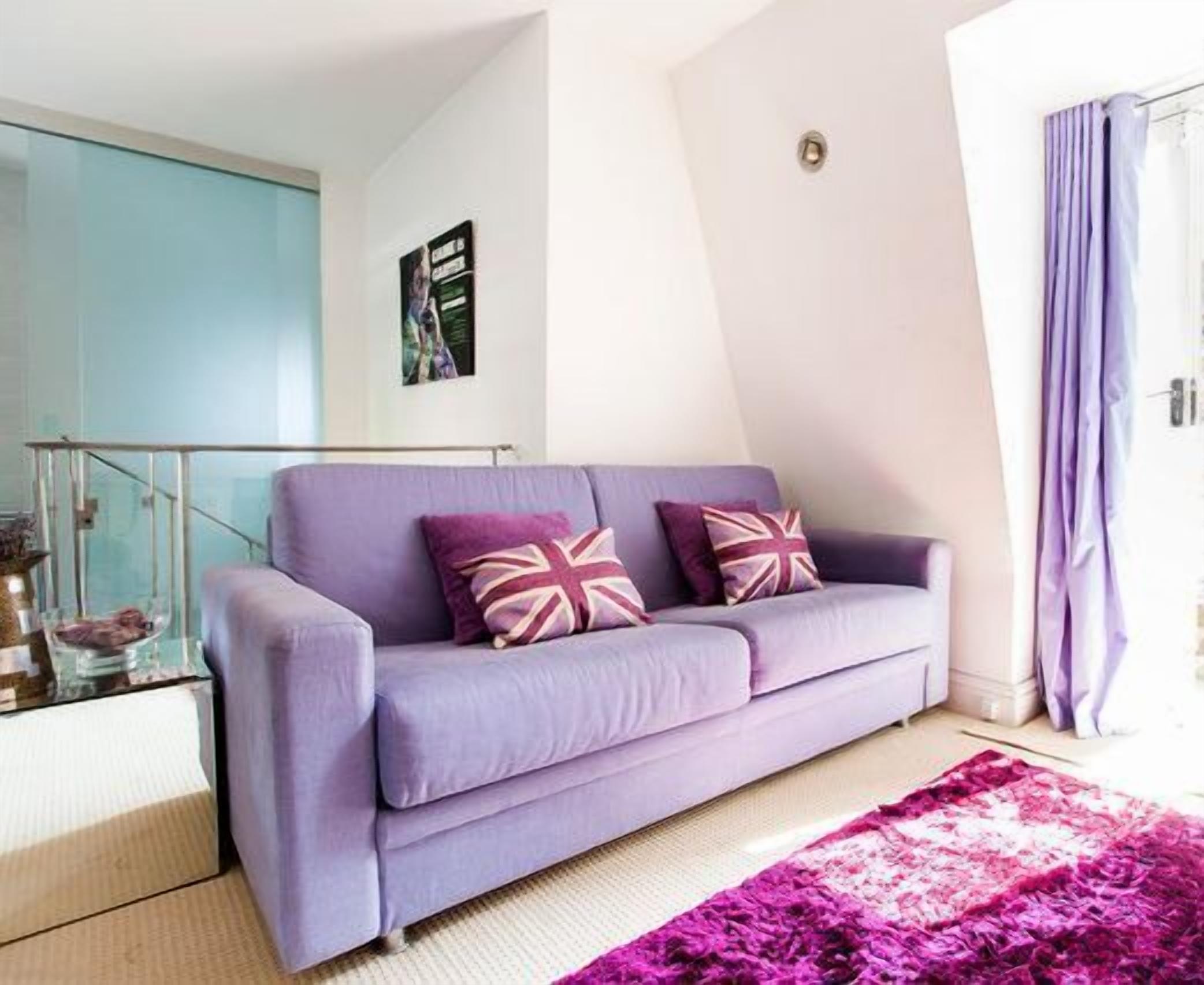 A modern living room with a purple sofa, a glass coffee table, and a vibrant purple rug.