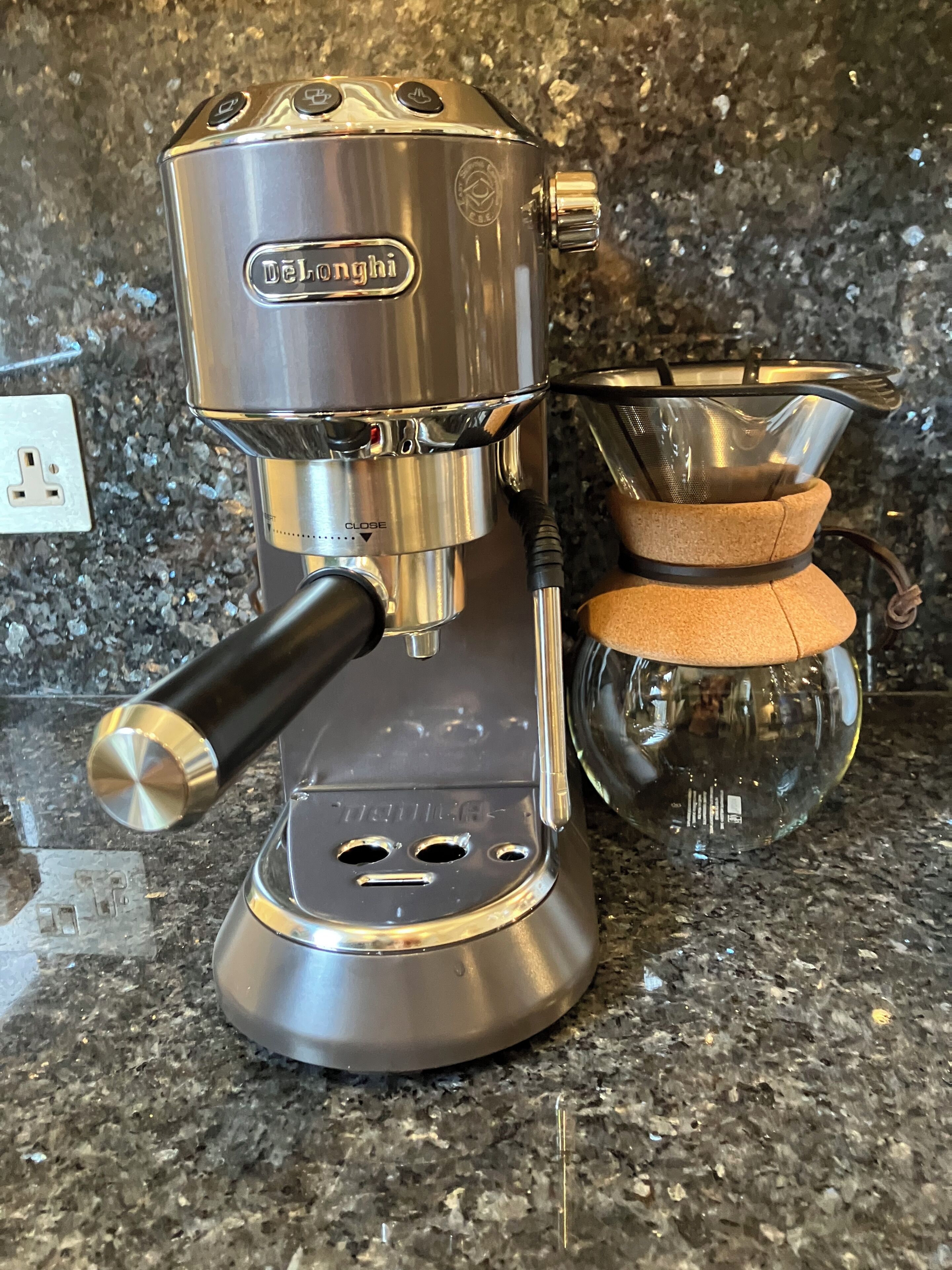 A DeLonghi espresso machine with a built-in grinder, a portafilter, and a tamper on a granite countertop.