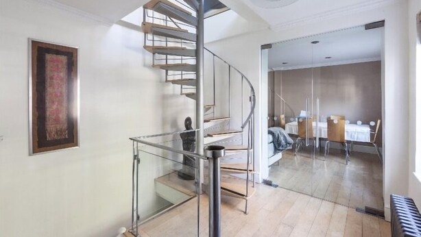 A modern interior with a spiral staircase, a dining area with tables and chairs, and a large framed artwork on the wall.