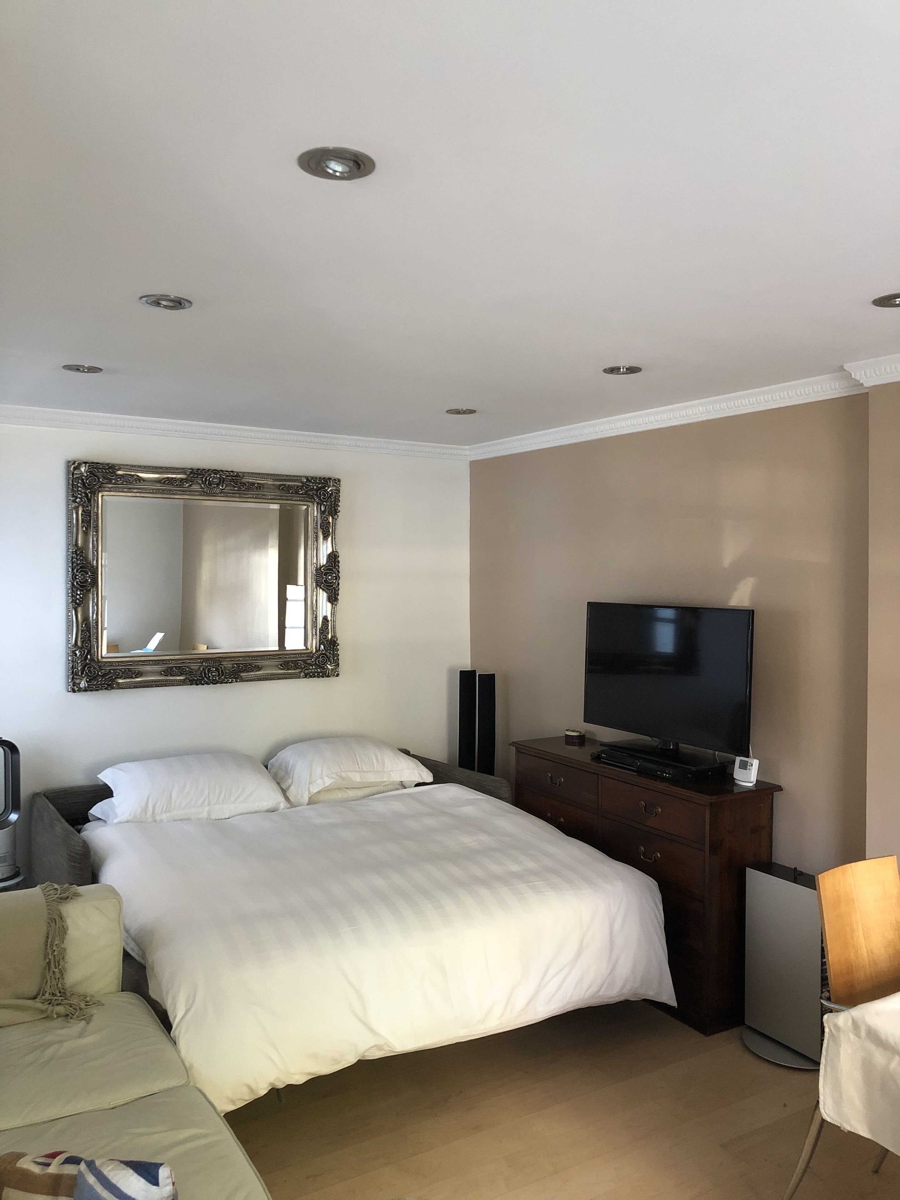 Una habitación de hotel con una cama grande, un televisor sobre un aparador de madera, un espejo y una lámpara.