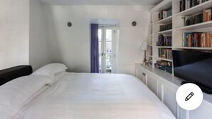 A hotel room with a bed, a bookshelf, and a window with curtains.