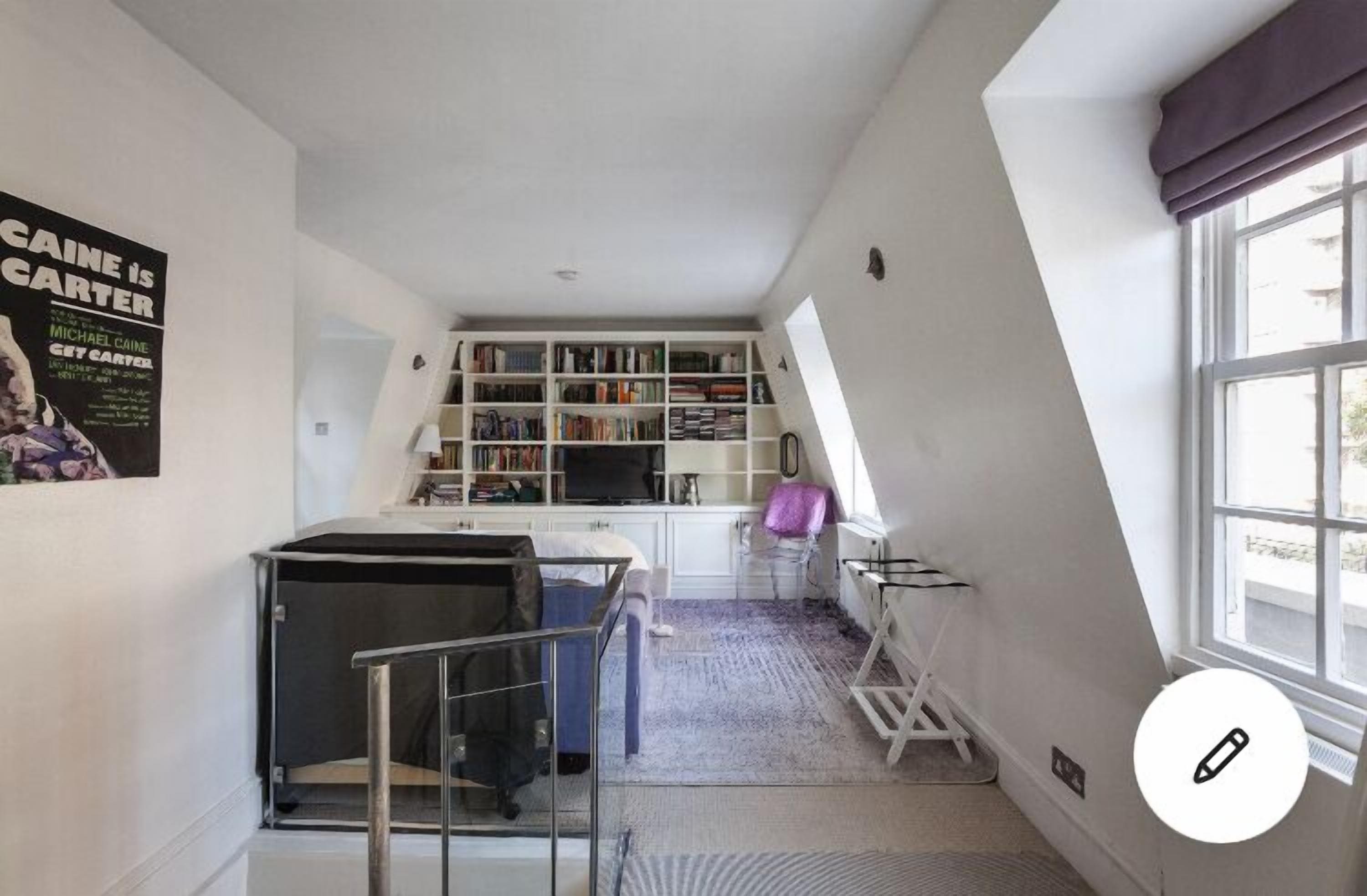 Une pièce compacte et bien éclairée, dotée d’une bibliothèque intégrée, d’un bureau avec une chaise et d’une fenêtre avec des rideaux.