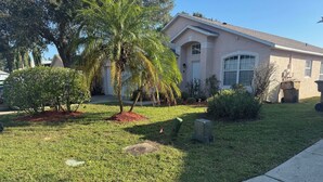 A residential property with a well-maintained lawn, a palm tree, and a house with a beige facade and large windows. - Luxury Villa with Private Pool 8 miles from Disney & near golf (CLERMONT)