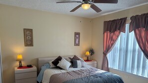 A bedroom with a bed, two bedside tables with lamps, a ceiling fan, and a window with curtains. - Luxury Villa with Private Pool 8 miles from Disney & near golf (CLERMONT)