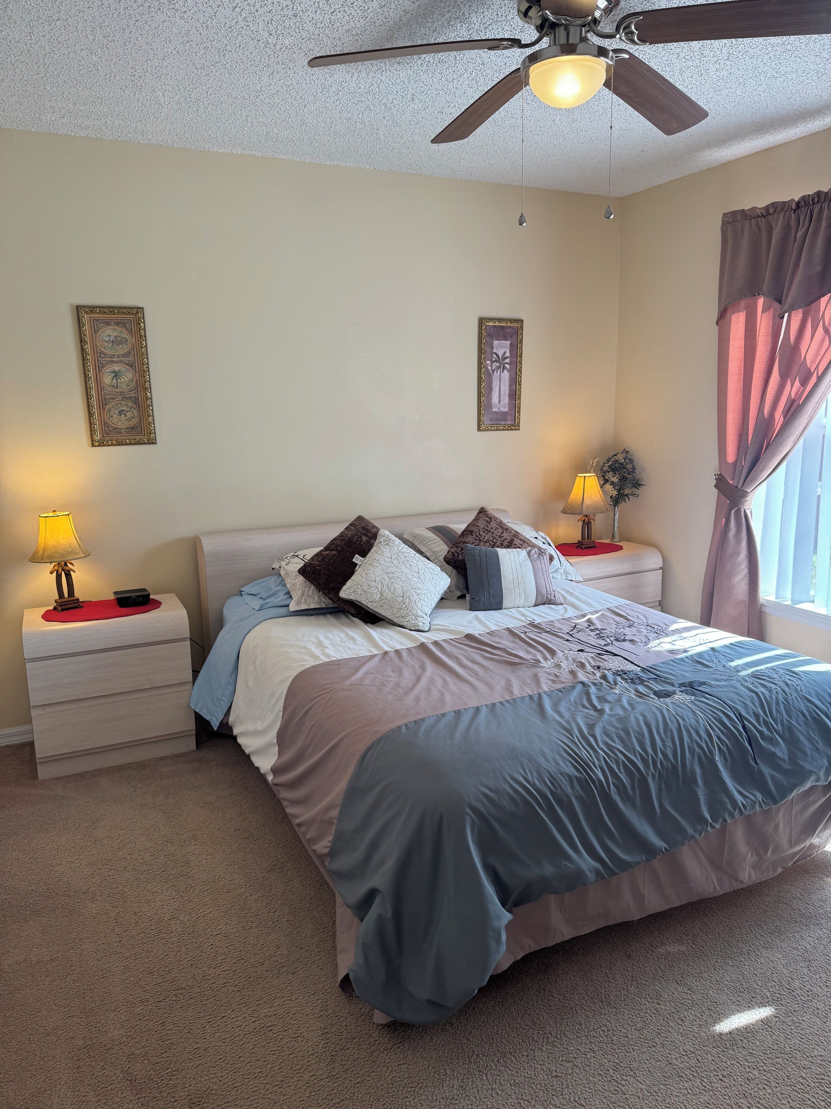 A bedroom with a bed, nightstands, a ceiling fan, and wall art.