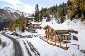 Eine Holzhütte mit Balkon, umgeben von schneebedeckten Bäumen und Bergen.