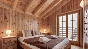 Un dormitorio con paneles de madera, una cama grande, dos mesitas de noche con lámparas y un ventanal con vidrio esmerilado.