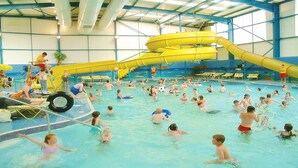 A large indoor swimming pool with multiple lanes, a water slide, and a lifeguard stand. - Stunning Romantic Cottage ★ nr Beach & Attractions ★Large Garden ★ Pet Friendly! (Chapel Saint Leonards)