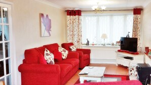 A living room with a red sofa set, a coffee table, a TV, and a window with curtains. - Stunning Romantic Cottage ★ nr Beach & Attractions ★Large Garden ★ Pet Friendly! (Chapel Saint Leonards)