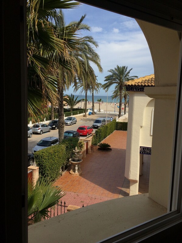 Vista de un estacionamiento con varios coches, palmeras y una playa al fondo.
