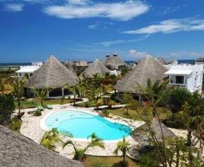 Un resort con cabañas de techo de paja, una piscina y vista al océano.