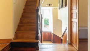 Un escalier en bois avec une rampe, menant à une pièce dotée d’une porte et d’un luminaire.