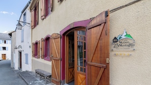Un bâtiment avec des volets en bois, un banc à l’extérieur et une enseigne indiquant qu’il s’agit d’un hôtel appelé « La petite Maison des 25 Montagnes ».