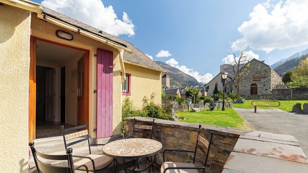Une terrasse avec une table ronde et des chaises, un mur en pierre et un bâtiment avec une porte rose.