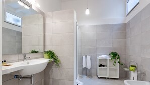 A modern bathroom with a large sink, a shower, and a bathtub. There are plants and a towel rack visible. - Grotta Pinta 7 | Cozy and romantic (Roma)