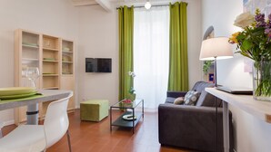 A modern living room with a sofa, a dining table with chairs, a TV, and a green curtain. - Grotta Pinta 7 | Cozy and romantic (Roma)