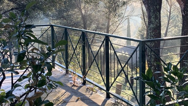 A metal railing overlooking a forested area with trees and a clear sky.