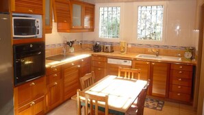 A kitchen with wooden cabinets, a microwave, an oven, a sink, and a dining table with chairs.